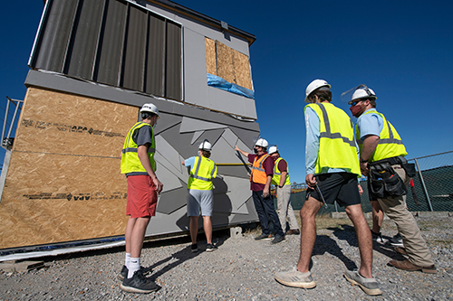 MSU Building Construction Science students and faculty stand near a modular building under blue skies.