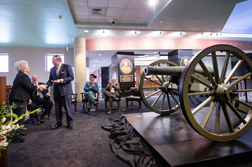A large cannon is on display as Frances Coleman hands a miniature replica cannon to Mark Keenum.