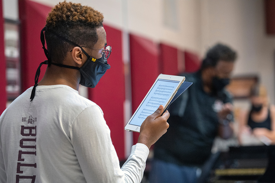 A student reads music on a tablet during an evening choir rehearsal led by MSU Professor Gary Packwood, who is pictured in the distance