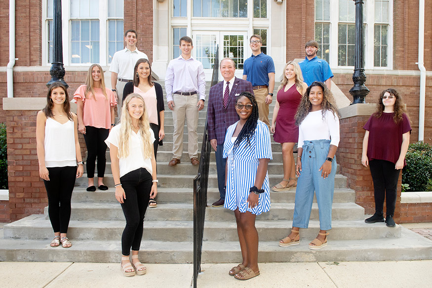 A dozen students stand on the steps of Lee Hall along with MSU President Mark Keenum