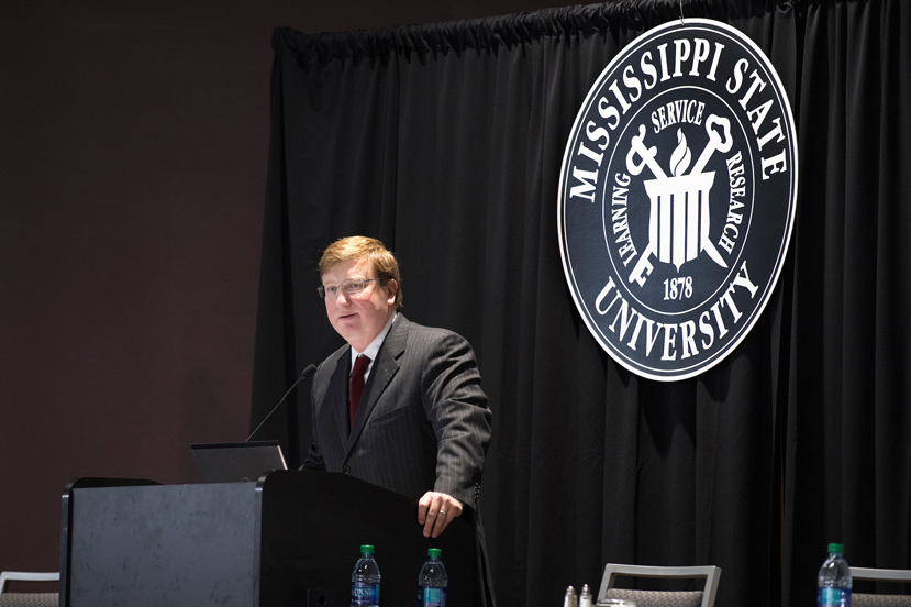 Mississippi Lt. Gov. Tate Reeves speaks during Friday’s [Dec. 9] Consumer Credit Symposium at The Mill at MSU Conference Center. Reeves is wearing a dark suit with maroon tie at a podium with MSU seal backdrop.(Photo by Beth Wynn) 