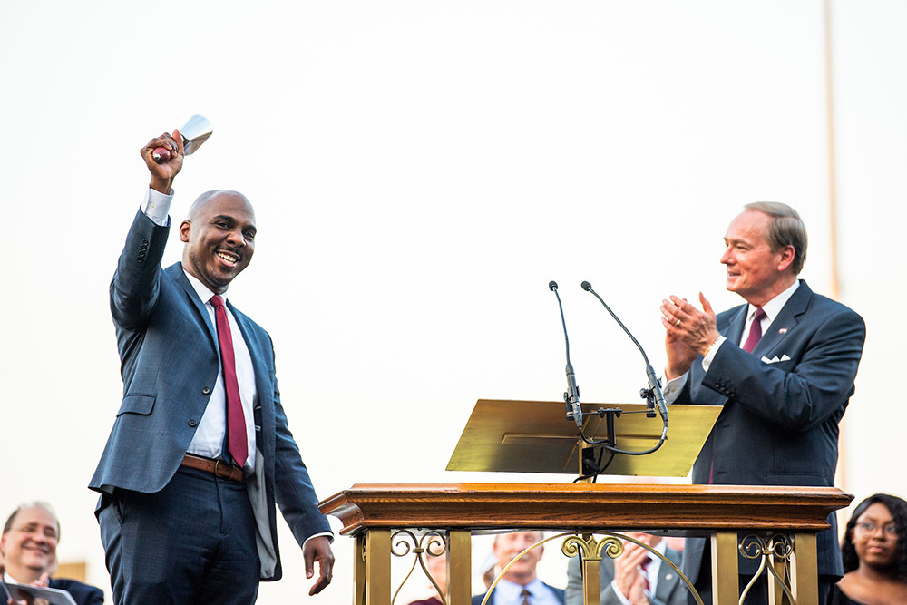 Stanley Blackmon rings a cowbell as Mark Keenum claps on the stage at convocation