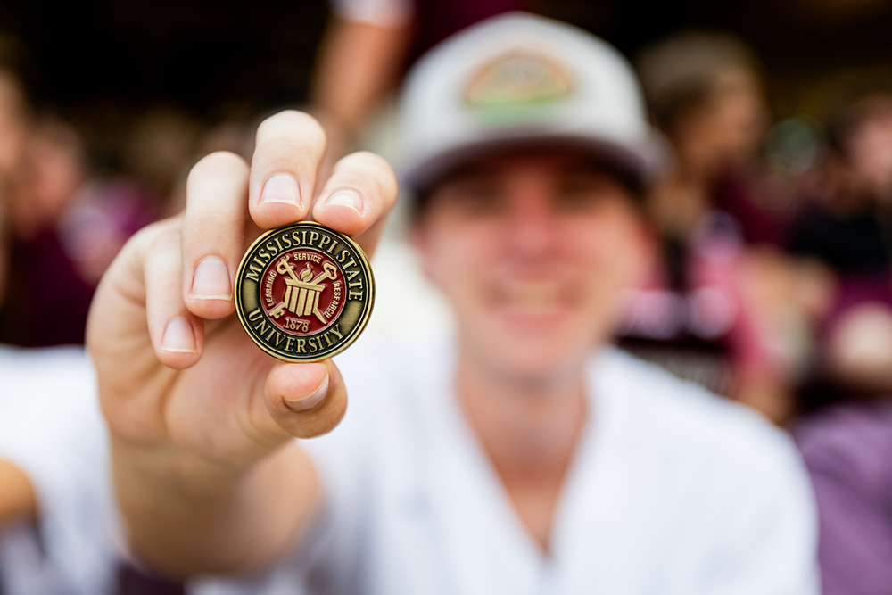 A student holds the commemorative convocation coin, which includes the MSU seal.