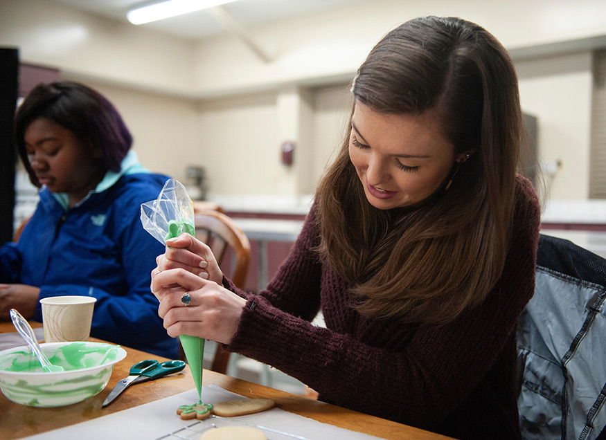 A woman decorates a cookie with green icing