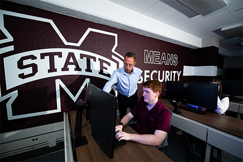 An MSU faculty member looks over as a student works in the cybersecurity lab