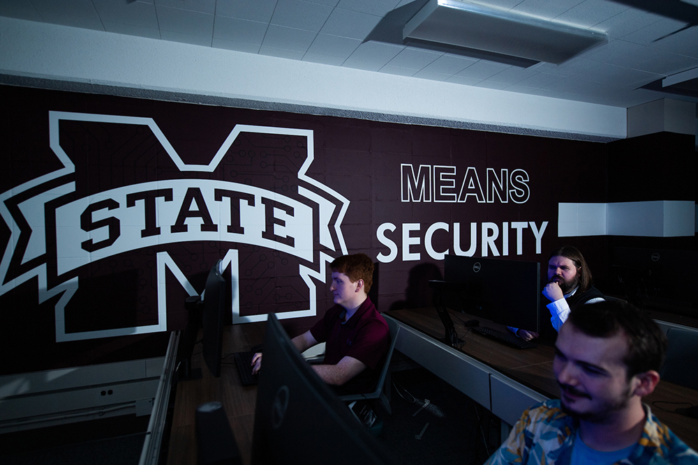 Students work in a lab in front of a graphic that reads "MSU Means Security"