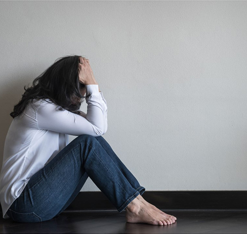 Woman pictured with her head in her hands while seated in front of a wall