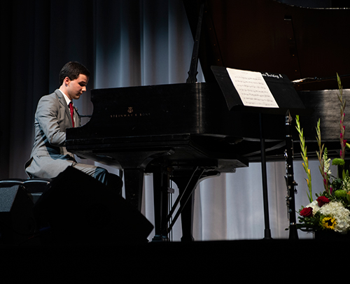 MSU student Daniel Rorabaugh is pictured seated on stage at a Steinway & Sons piano.