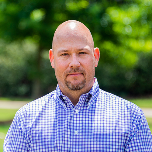 Portrait of Darrin Dodds outside with green foliage in the background.