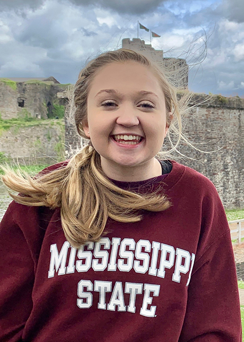 Lindsey Downs smiles while wearing a maroon Mississippi State sweatshirt in front of Caerphilly Castle in South Wales