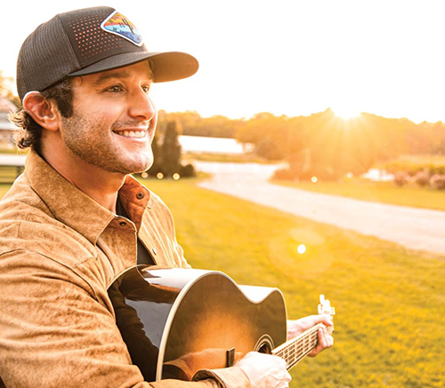 Musician Easton Corbin smiles while strumming a guitar on a sunny day.