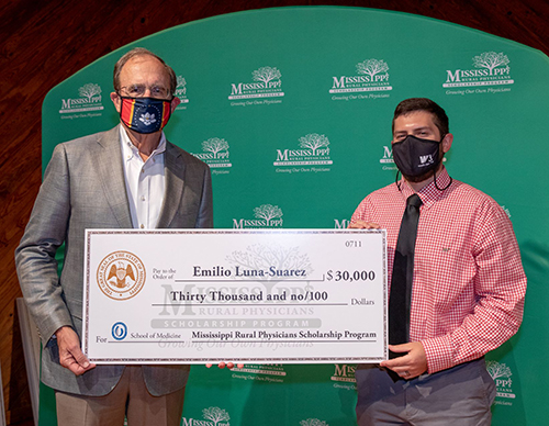 Lt. Gov. Delbert Hosemann and MSU graduate Emilio Luna-Suarez wear face masks while holding a $30,000 check from the Mississippi Rural Physicians Scholarship Program.