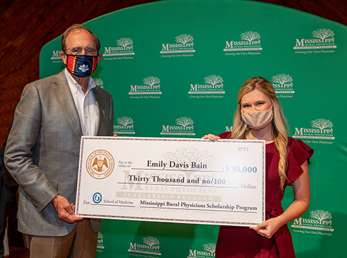 Lt. Gov. Delbert Hosemann and MSU graduate Emily Davis Bain wear face masks while holding a $30,000 check from the Mississippi Rural Physicians Scholarship Program.