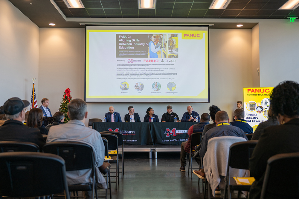 A panel discussion with participants seated at a table in front of a large screen