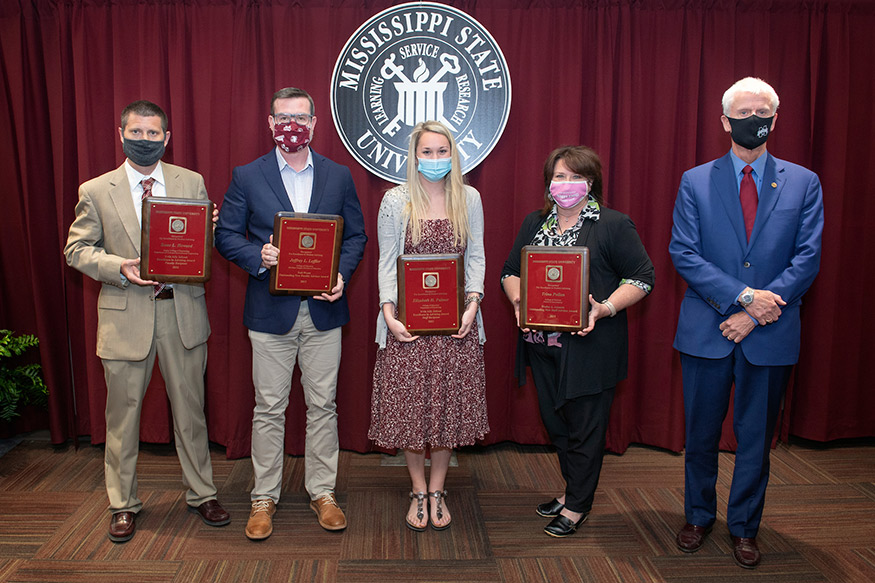 Four faculty and staff advising honorees holding awards stand with MSU Executive Vice Provost Peter Ryan in front of the MSU seal. 