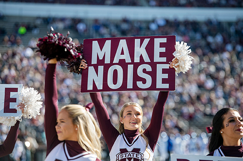 An MSU cheerleader holds up a sign that says "Make Noise" during a football game