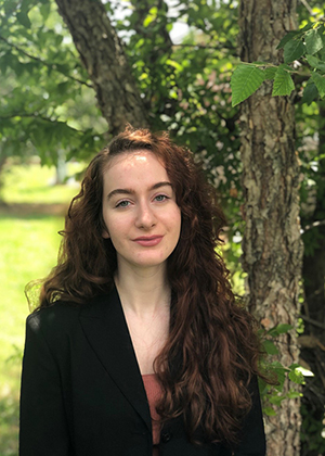 Zoe Fowler wears a black blazer and stands in front of a tree near a grassy field.