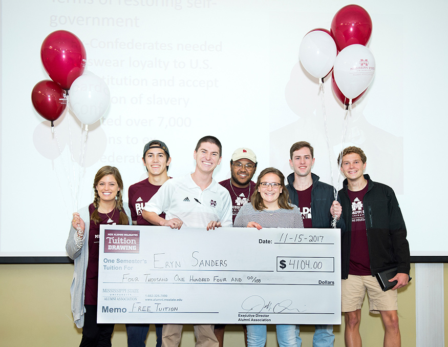 Eryn Sanders (holding check, at right), a freshman kinesiology major from Belden, is surprised during class with a check for spring tuition after winning the MSU Alumni Association’s free tuition drawing. She was presented with the check by MSU Alumni Delegates, from left, Elizabeth Shapley, Nolan Cannon, Will Basden, Quin Gray, Jon Stockton and William Johnson. (Photo by Russ Houston) 