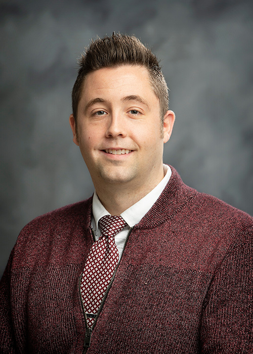 A studio portrait of Daniel Gadke wearing a maroon tie and sweater.