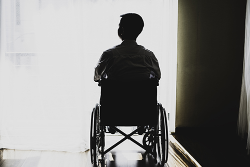 A man in a wheelchair is pictured in front of a brightly lit window.