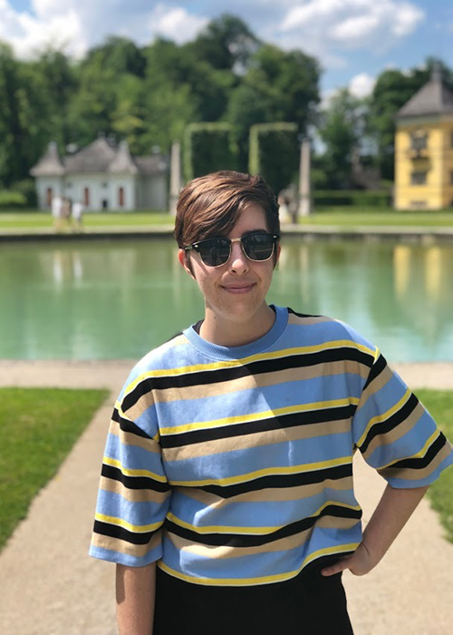 Grace Barnes is pictured wearing sunglasses while standing in front of a lake with trees and houses in the background.