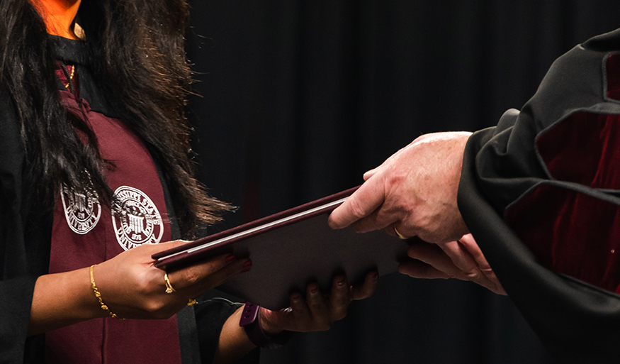 A close-up picture of a diploma cover being handed to a graduating student