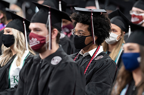 Graduates wearing masks sit in MSU's Humphrey Coliseum during spring commencement ceremonies.