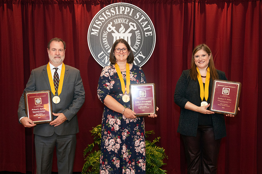 Three faculty members stand holding Grisham Master Teacher awards.