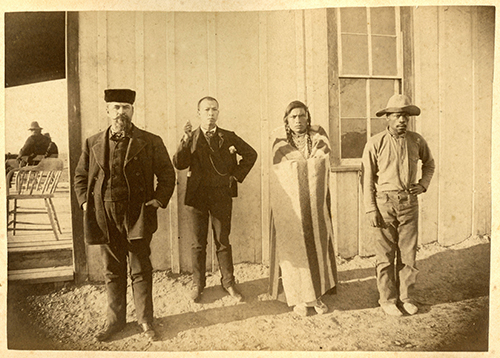 Photograph of a white man, possibly Dr. A.B. Holder, an unidentified Chinese man, an unidentified member of the Apsaalooke (Crow) tribe, and a Black cowboy, possibly Charles “Smoky” Wilson