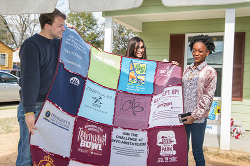 Mississippi State University students Rob Montgomery and Mariam Khmaladze present a handmade t-shirt quilt to Kareema Gillon. The quilt is designed to help the Gillon family remember the MSU students that worked on the new home, which was dedicated to the Gillons on Tuesday [Nov. 21]. (Photo by Beth Wynn)
