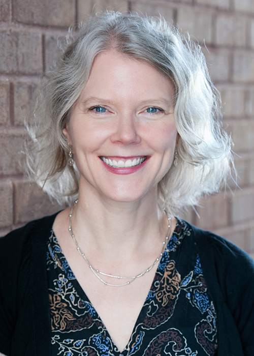 Becky Hagenston smiles for the camera while standing in front of a brick wall.