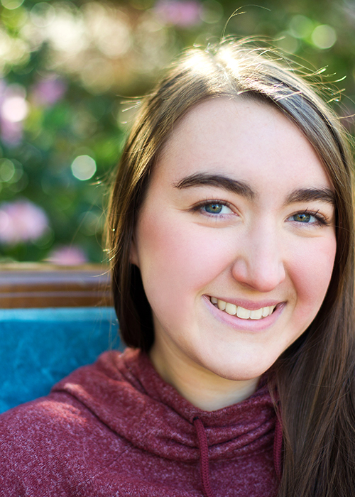 Hannah Scheaffer smiles for the camera while seated in a blue-cushioned chair.