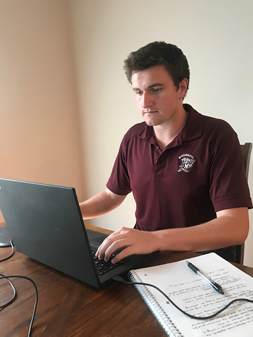 MSU senior electrical engineering major Hugh Coleman is pictured wearing a maroon polo and seated at his gray laptop in front of a beige wall.