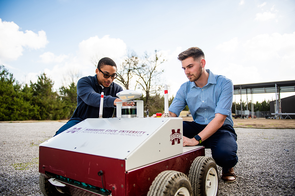 Two students adjust an autonomous robot in an outdoor setting