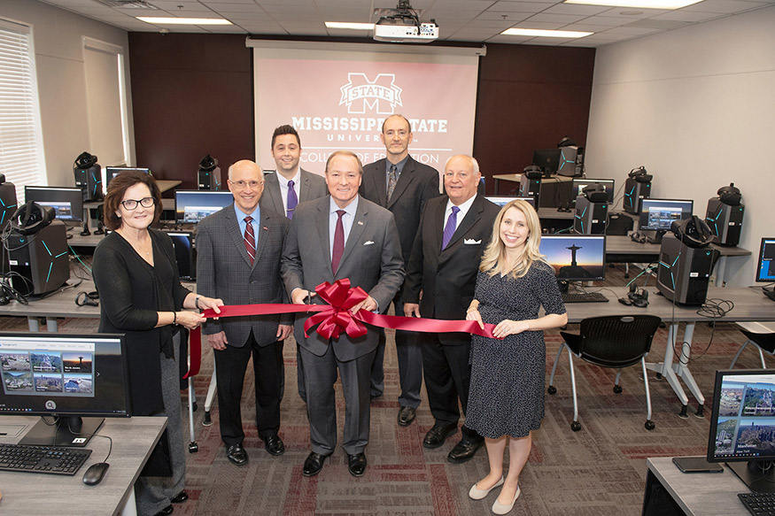 MSU leaders pose holding a ribbon to celebrate the opening of the College of Education’s new Virtual Reality Academy and Lab with computer monitors and other technology tools in the background.