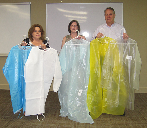 Debbie Miller, Susan Moore and John Moore hold up isolation gowns.