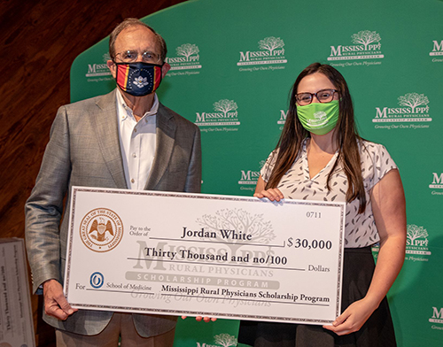 Lt. Gov. Delbert Hosemann and MSU graduate Jordan White wear face masks while holding a $30,000 check from the Mississippi Rural Physicians Scholarship Program.
