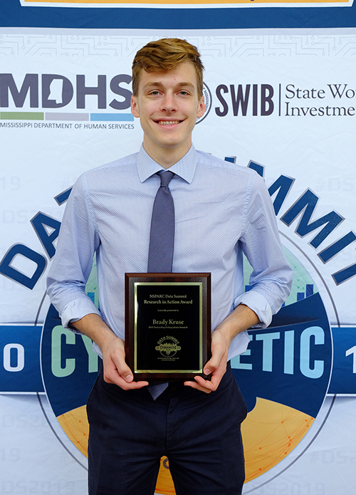 Brady Kruse holds an award in front of the Data Summit backdrop