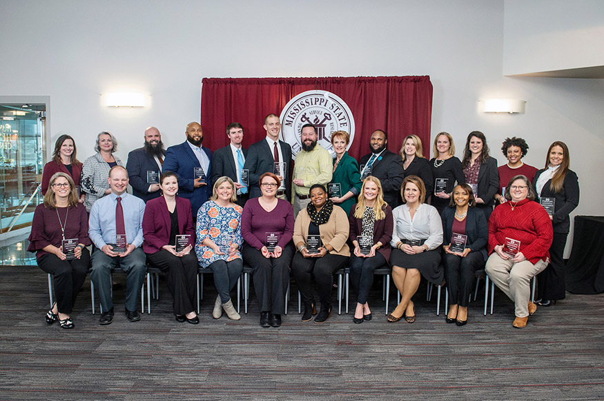 Two rows of men and women hold their LEAP awards in front of an MSU seal