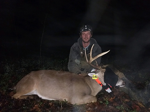 MSU master's student Luke Resop is pictured with a deer in a grassy area covered with leaves.