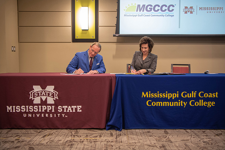 MSU President Mark E. Keenum and MGCCC President Mary S. Graham sign agreements while seated behind table draped with MSU and MGCCC tablecloths, respectively.