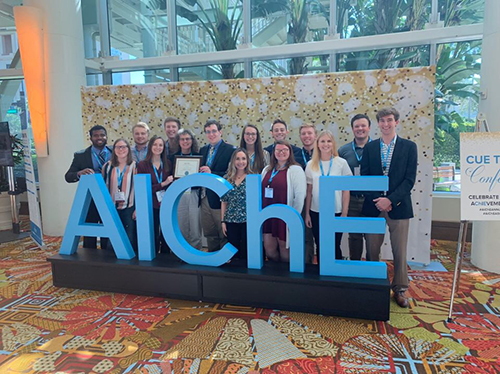 Members and adviser of MSU’s AIChE chapter smile for a group photo near a large AIChE sign at the organization’s annual student conference.