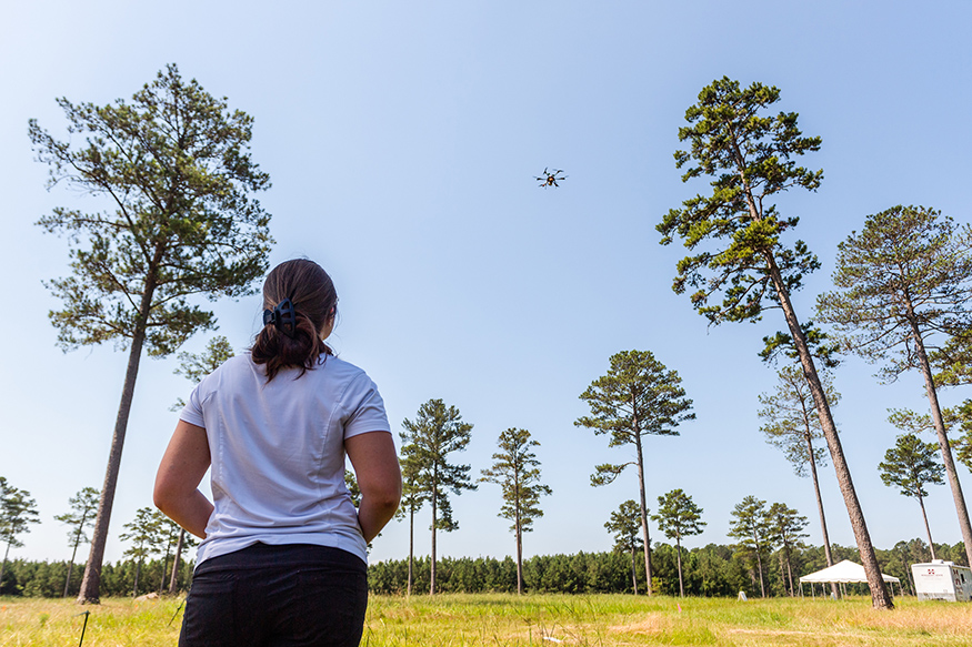 A female student operates a small drone in a forest setting.