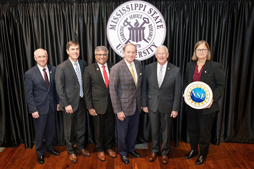 Group photo in front of the MSU seal and holding an NSF logo