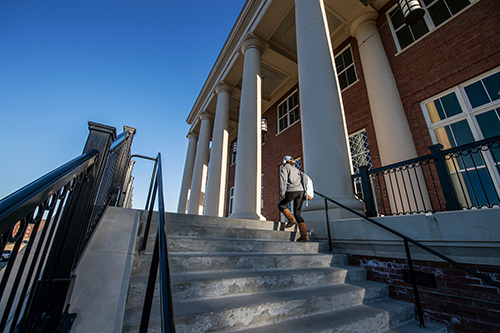 An MSU student ascends stairs at the front of the Old Main Academic Center. 