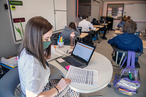 A student teacher works from her desk in a middle school classroom