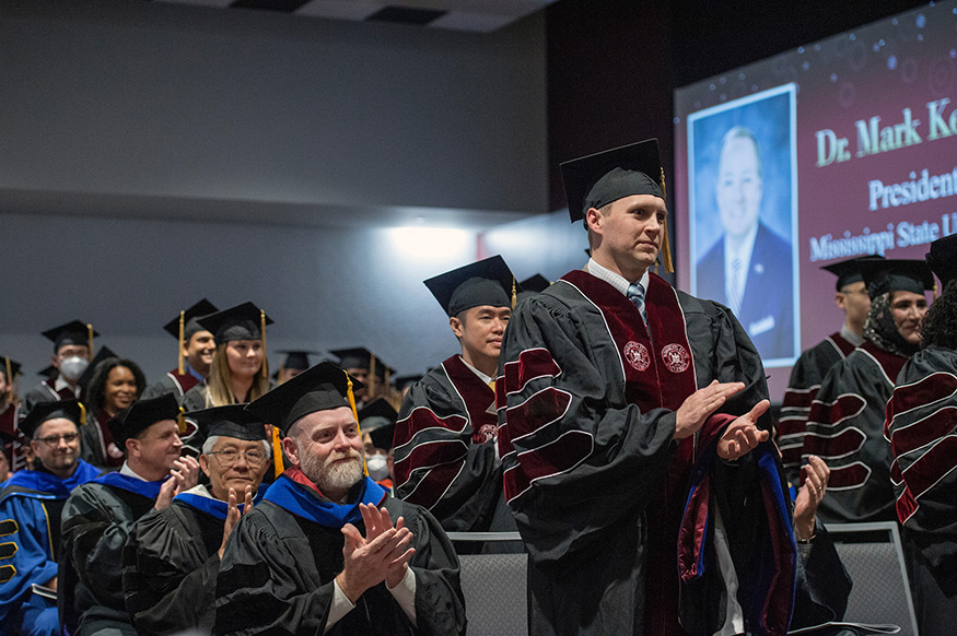 People wearing regalia applaud during the Doctoral Hooding Ceremony