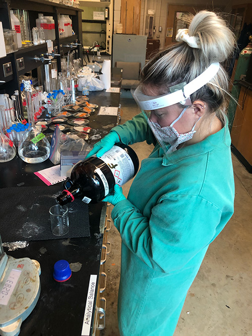 A young woman works in a chemistry lab while wearing protective equipment