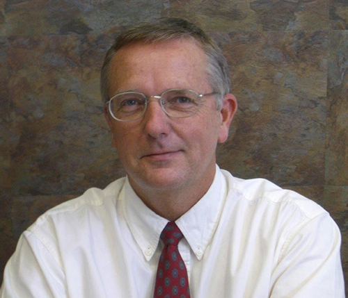 Studio headshot of Randy Bell wearing a white shirt in front of a gray background