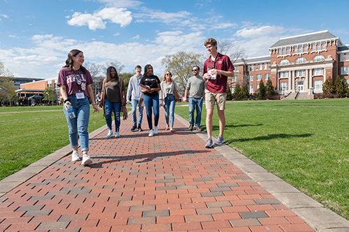 A group of students and parents walk on the Drill Field during a campus tour with a Roadrunner